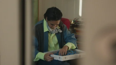 Shruti Ganguly rummaging through a box of puzzle pieces while sitting down.